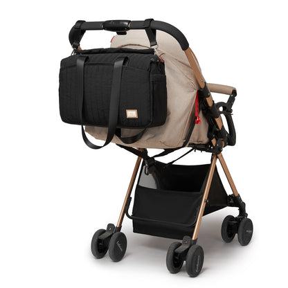 Black diaper bag mounted on beige stroller handlebar using dedicated trolley sleeve